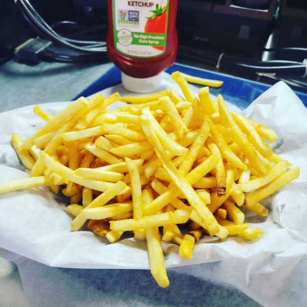A large serving of golden french fries in a paper-lined basket with a ketchup bottle in the background.