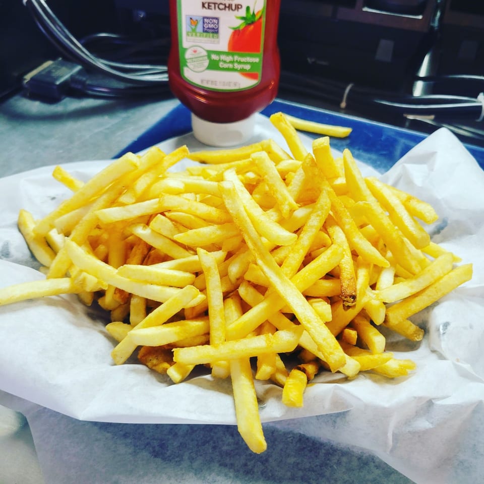 A large serving of golden french fries in a paper-lined basket with a ketchup bottle in the background.