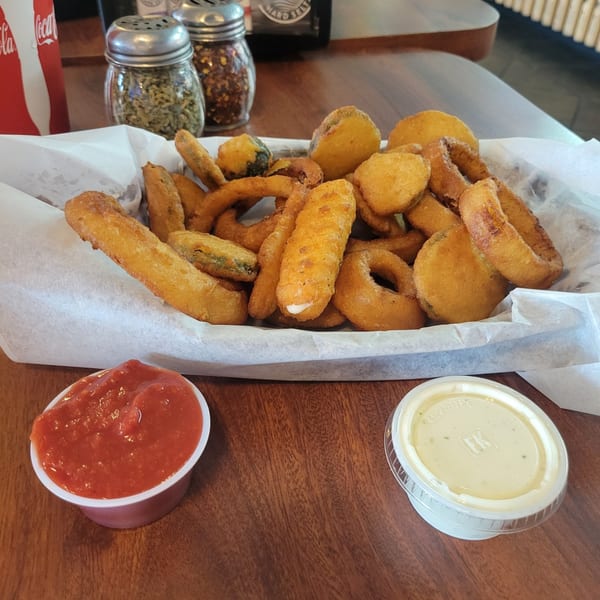 A basket of fried appetizers, including onion rings, mozzarella sticks, and fried pickles, with ketchup and ranch.
