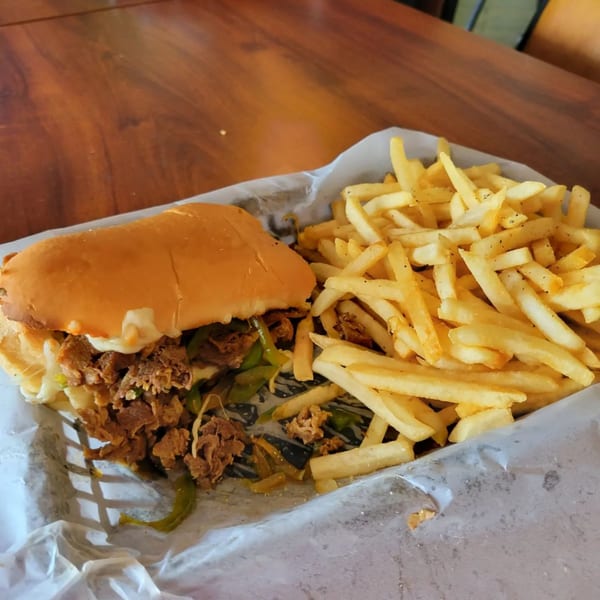 Ballpark Pizza & Subs cheesesteak sub with green peppers and onions, served with a side of fries.