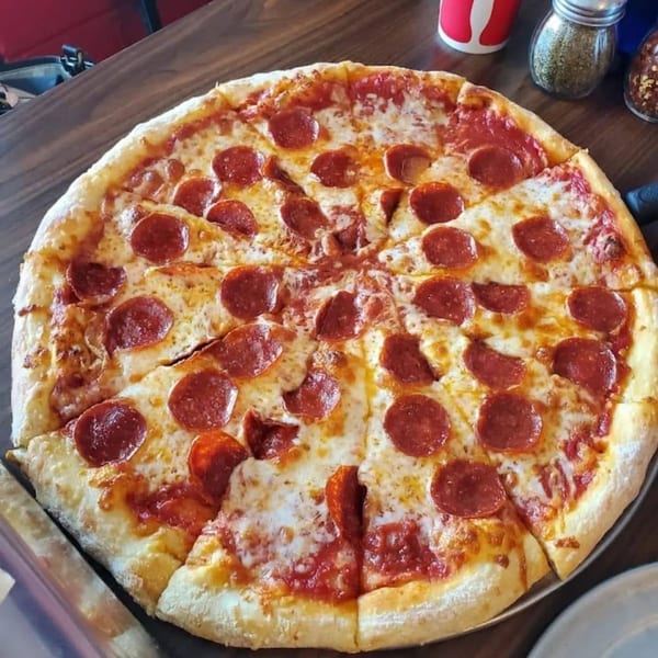 A large, freshly baked pepperoni pizza with melted cheese and tomato sauce on a wooden table.