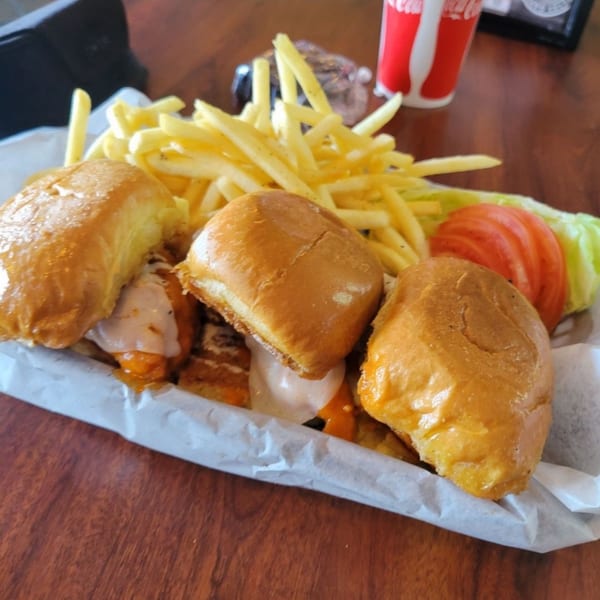 Three chicken sliders with melted cheese, a side of fries, lettuce, and tomato in a basket.