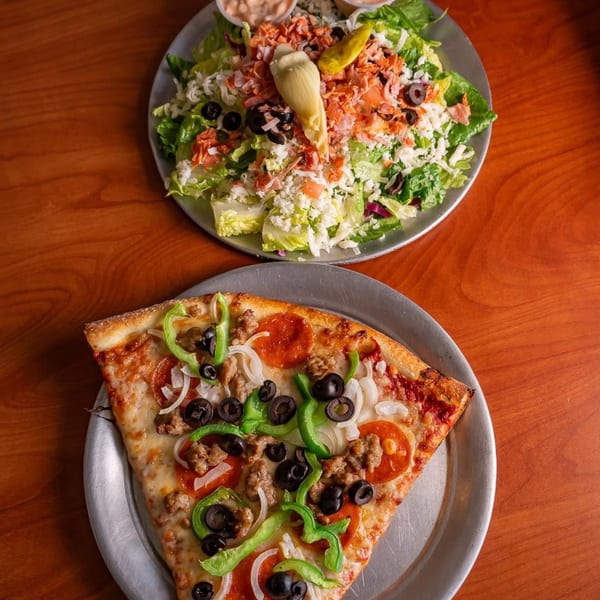 A slice of Ballpark Pizza with pepperoni, sausage, peppers, and olives, next to a large salad.